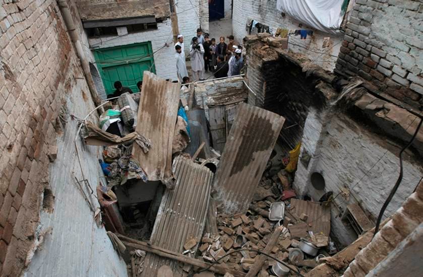 पाकिस्तान के पेशावर में भूंकप से ध्वस्त मकान के बाहर खड़े लोग। (फोटो-एपी)