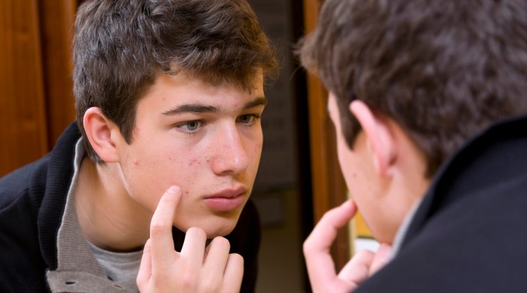 Teenager examining acne in the mirror