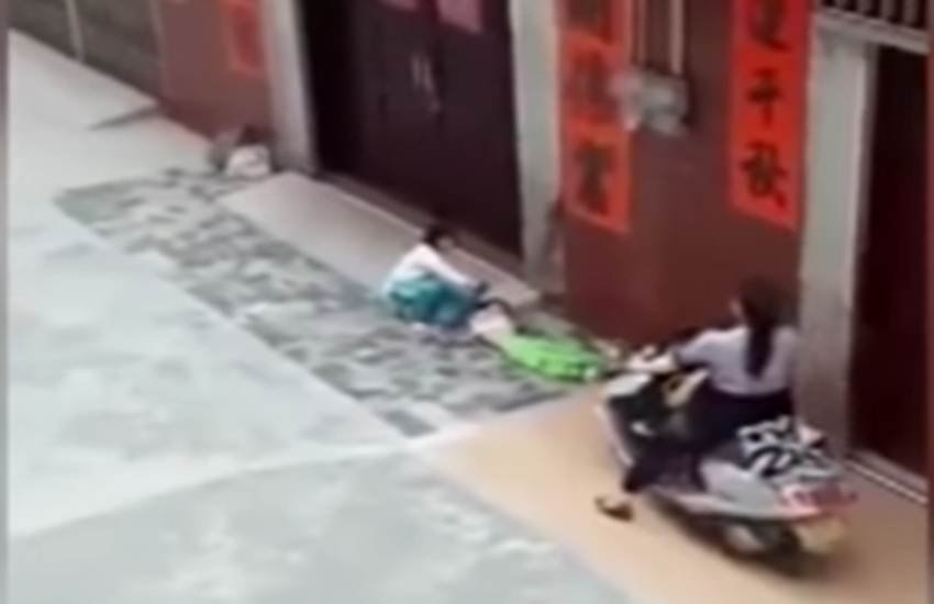 वीडियो में साफ-साफ दिख रहा है कि 6-7 साल की एक बच्ची पीड़ित बच्ची का पैर पकड़कर खींच रही है और आरोपी महिला उसके पैर पर मोटर बाइक चढ़ा रही है। (स्क्रीनशॉट)