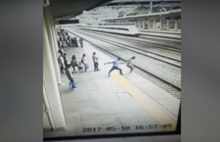 वह ट्रेक पर गिरने ही वाली होती है कि वहां खड़ा एक व्यक्ति उसे भागकर पकड़कर पीछे खींच लेता है। (Photo Source: CGTN Video Grab)