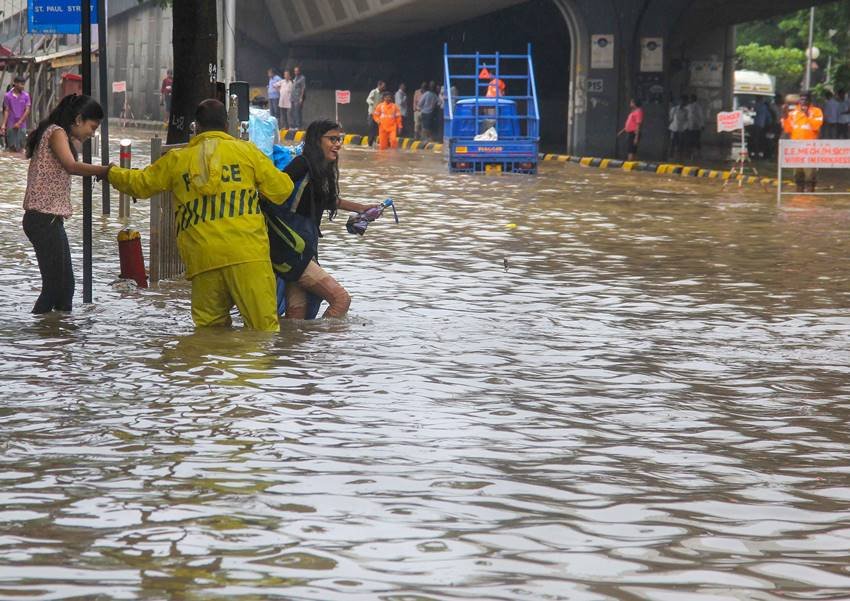 दो युवतियों को पानी से भरी सड़क को पार कराता व्यक्ति।
