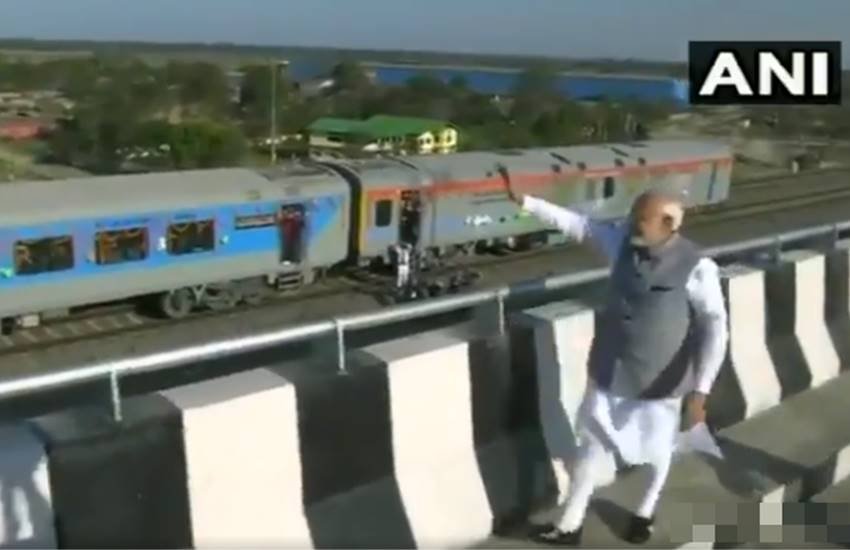 बोगीबील पुल से ट्रेन यात्रियों का अभिवादन स्वीकार करते पीएम नरेंद्र मोदी। (Image Grab from video tweeted by @ANI)