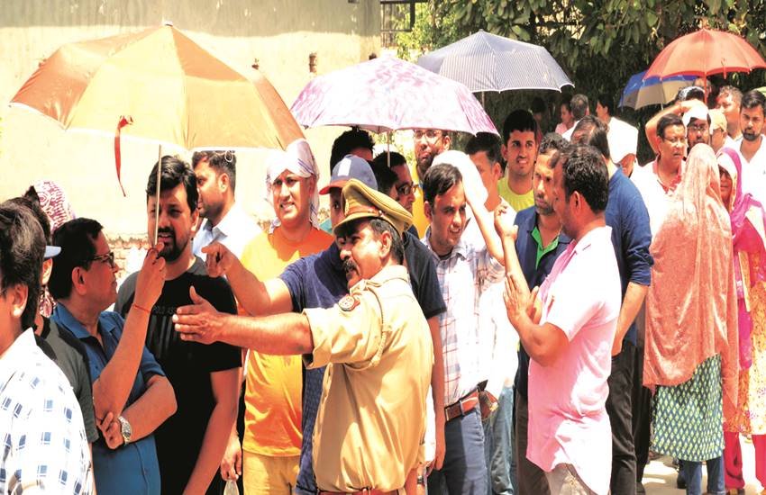 नोएडा स्थित एक मतदान केंद्र के बाहर कतार में खड़े मतदाता छतरी लगाकर खुद को धूप से बचाते हुए।