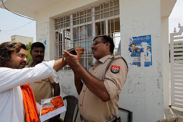 पुलिस अधिकारी को जीत की मिठाई खिलाता बीजेपी कार्यकर्ता।