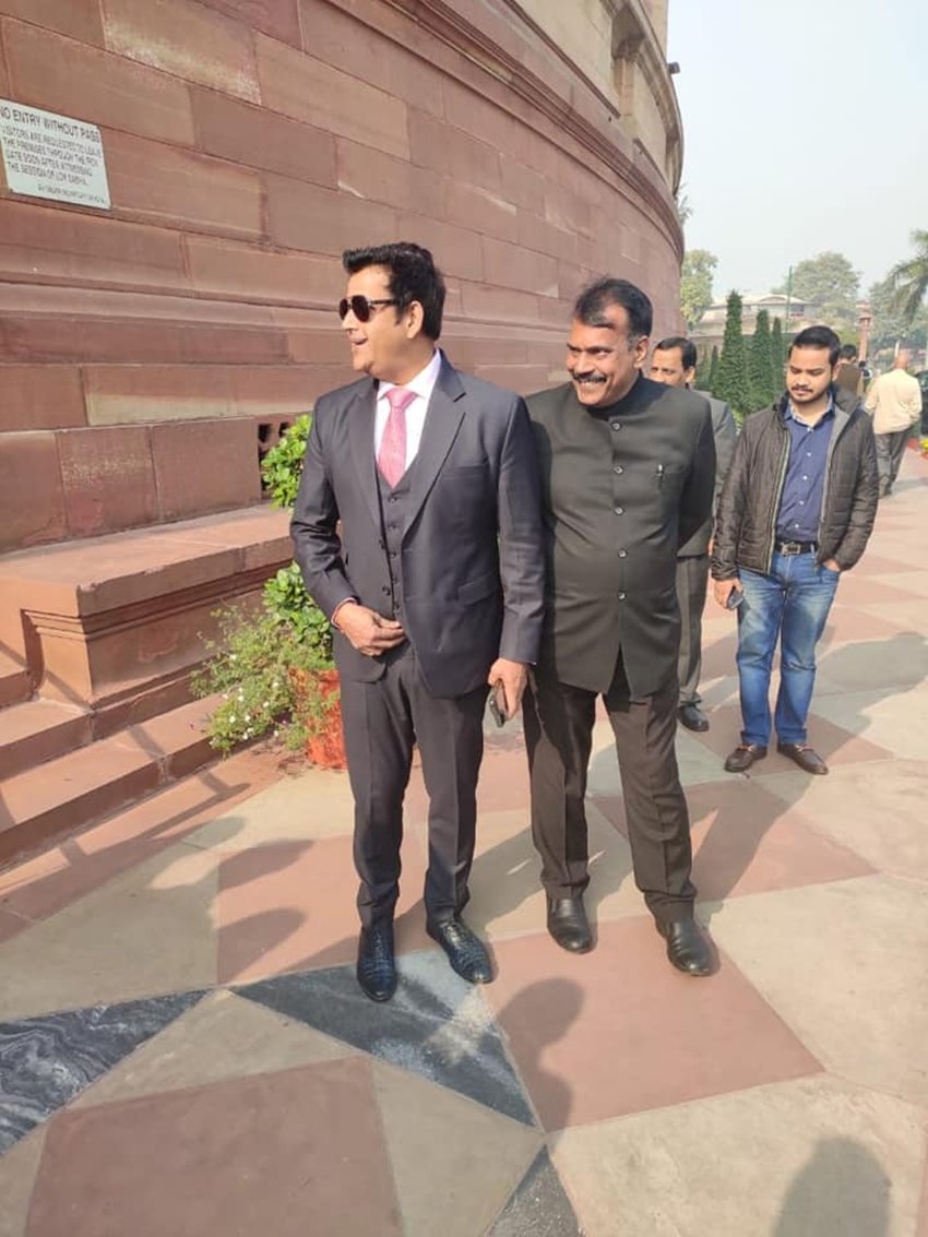 रवि किशन थ्री पीस सूट गुलाबी टाई और काले चश्मे में नजर आ रहे हैं।
