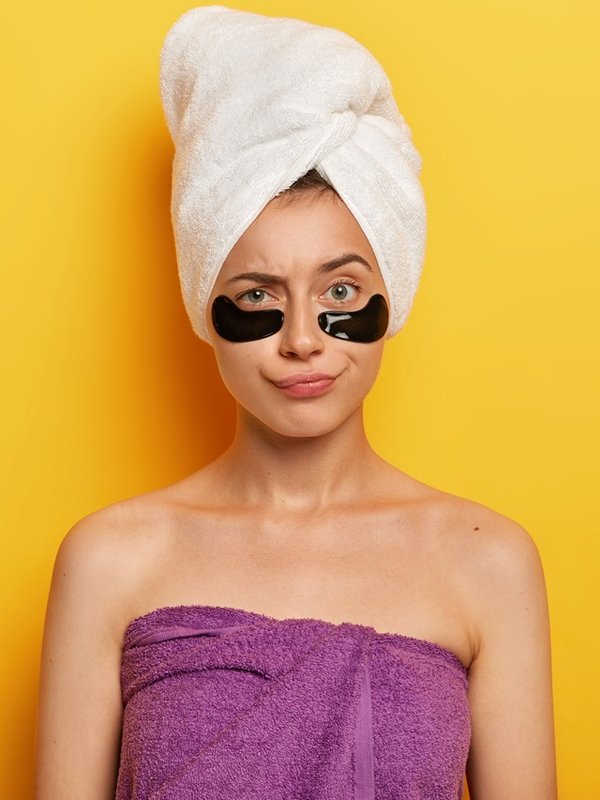 Daily pampering routine. Lovely young female model wears under eye circles for removing dark circles, takes care of her skin, uses modern cosmetics, stands against yellow studio wall, copy space aside