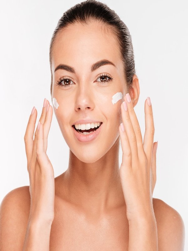 Beautiful young woman applying cosmetic cream treatment on her face