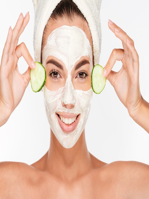 Beautiful woman applying cucumber on her face with cosmetic mask