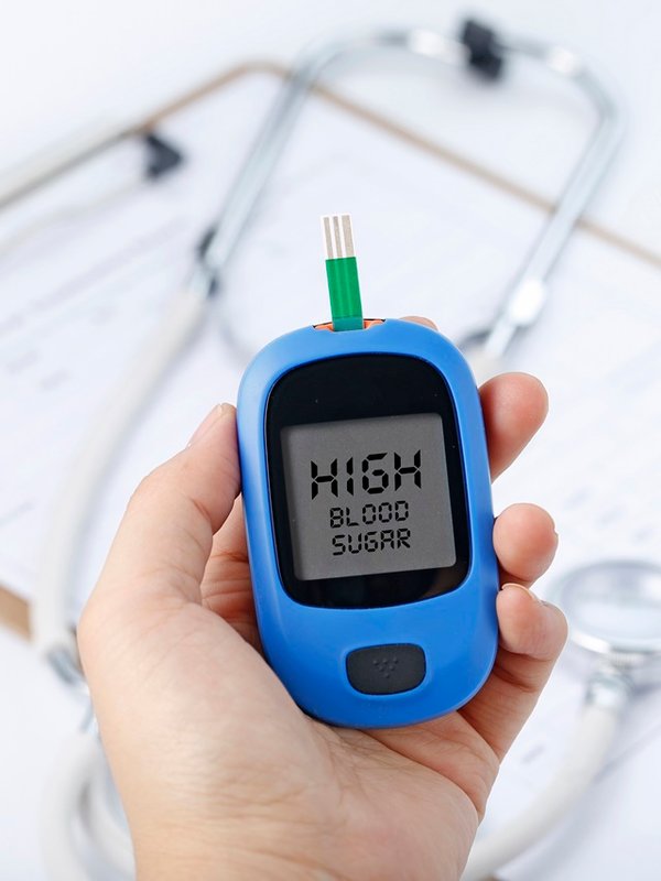 Hand holding a blood glucose meter measuring blood sugar, the background is a stethoscope and chart file