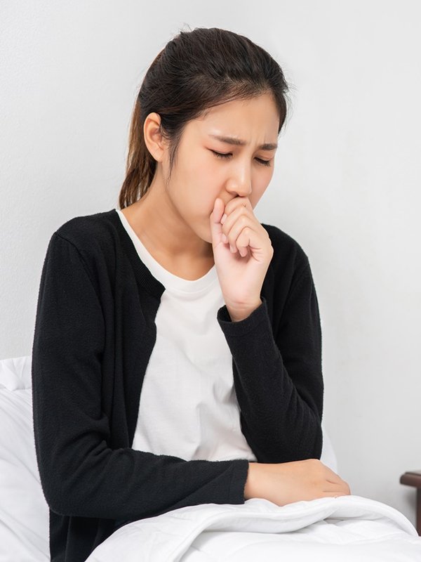 The woman coughed and covered her mouth with her hand and sat on the bed.
