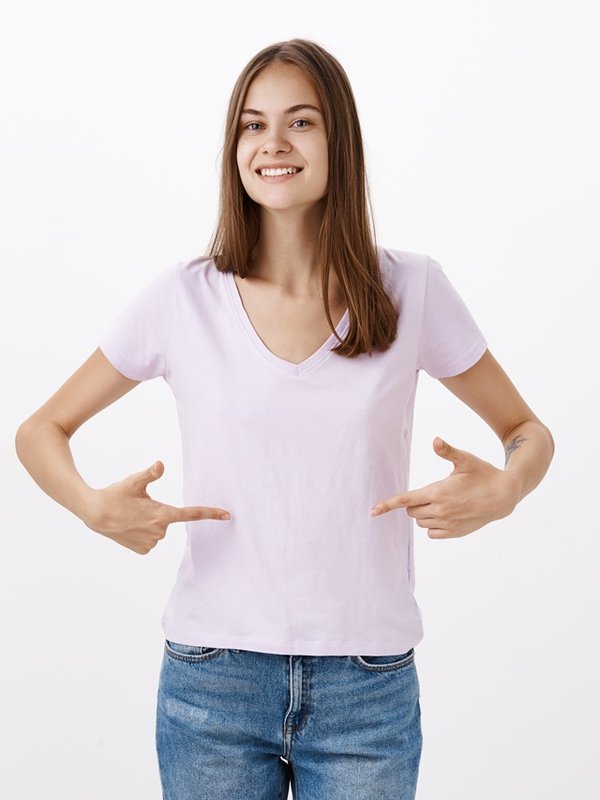 Cute young sportswoman giving advices how stay fit smiling joyfully gazing friendly at camera pointing at t-shirt or belly standing delighted and pleased with happy look over grey wall