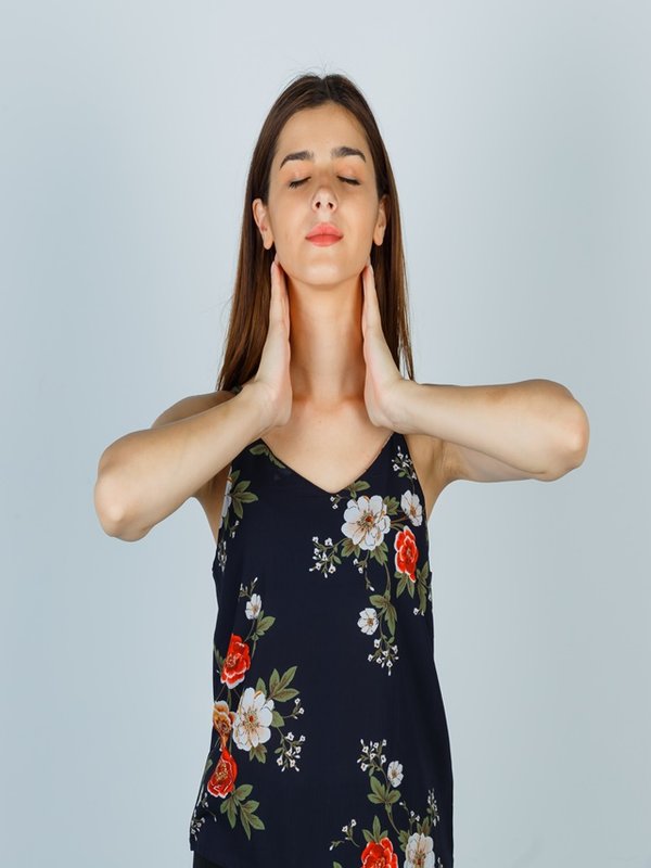Portrait of young lady touching her neck with hands in blouse and looking relaxed front view