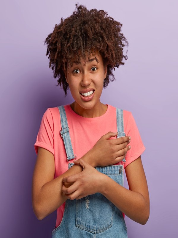 Skin problem and dermatology concept. Displeased curly African American woman scratches itch on arm, has allergy symptoms, sensitive skin, clenches teeth from unpleasant feelings. Annoying rash