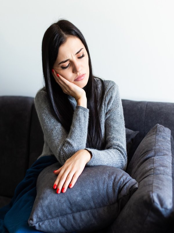 Indisposed sick woman feeling her temperature while resting on the sofa at home