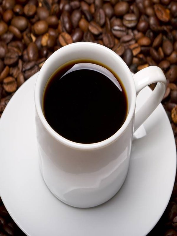 High angle shot of a white cup of black coffee on a surface full of coffee beans
