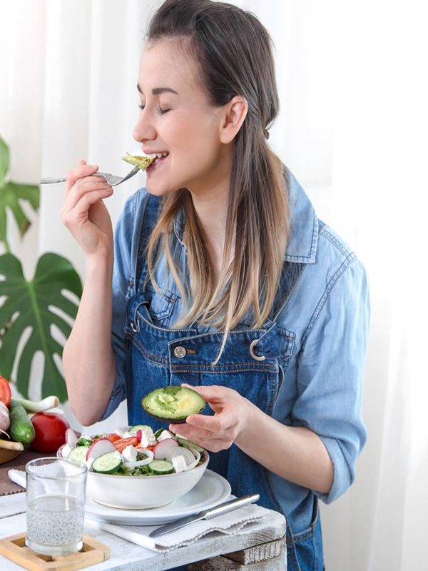 Young and happy woman eating salad at the table