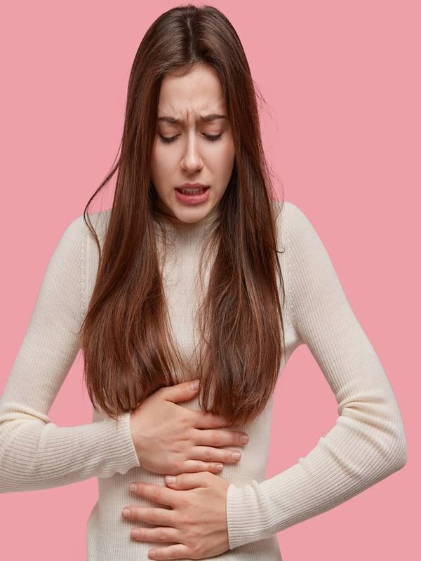 Image of unhappy woman suffers from stomachache after eating spoiled food, feels discomfort in belly, has disorder, wears casual clothes, models against pink background. Painful disease conccept