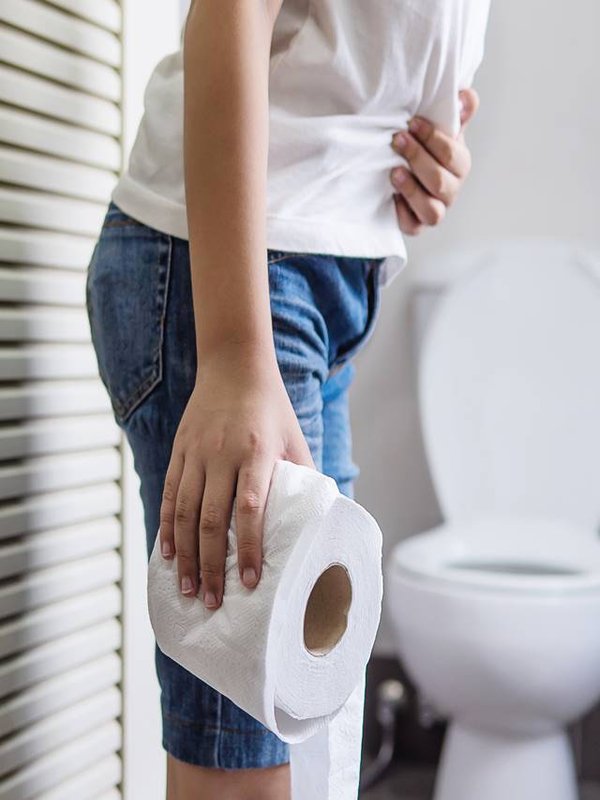 Asian boy sitting on toilet bowl holding tissue paper - health problem concept