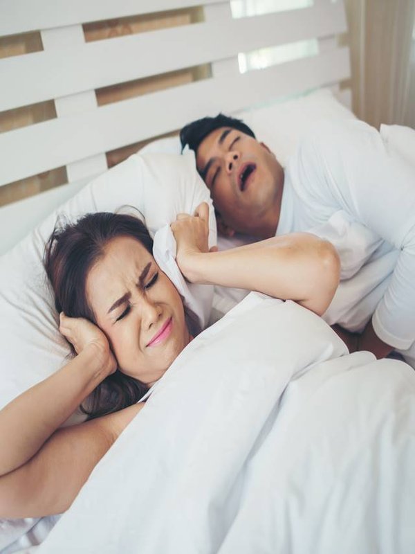 Portrait of woman blocking ears with man sleeping snoring on bed