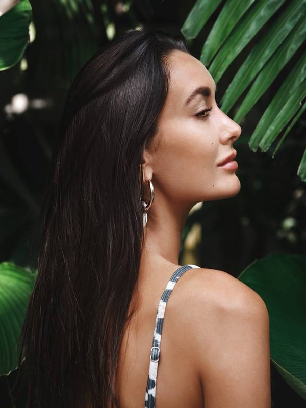 Tropical vacation and travelling concept. Rear view of beautiful brunette woman with golden tan, wearing bikini, standing in profile in green leaves, palm trees and tropic nature