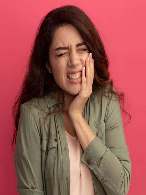 aching young beautiful girl wearing olive green t-shirt putting hand on aching tooth isolated on pink background