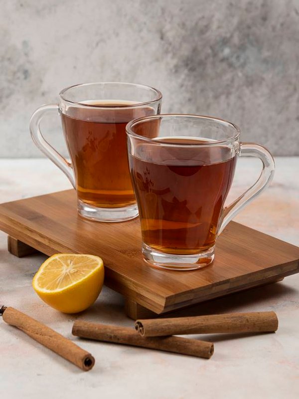 Two cups of hot tea on wooden board with cinnamon sticks