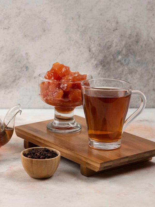 Cup of hot tea, teapot and sweet quince jam on wooden board