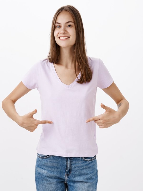 Cute young sportswoman giving advices how stay fit smiling joyfully gazing friendly at camera pointing at t-shirt or belly standing delighted and pleased with happy look over grey wall