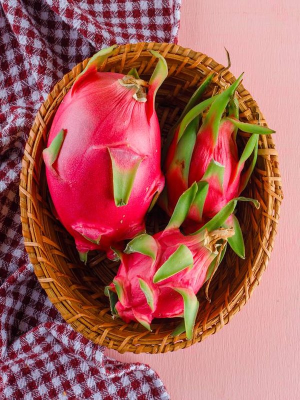 Dragon fruit in a wicker basket on pink and picnic cloth background, flat lay.