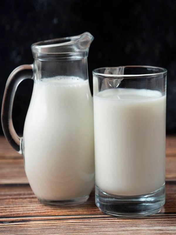 Fresh milk in a mug and jug on wooden table