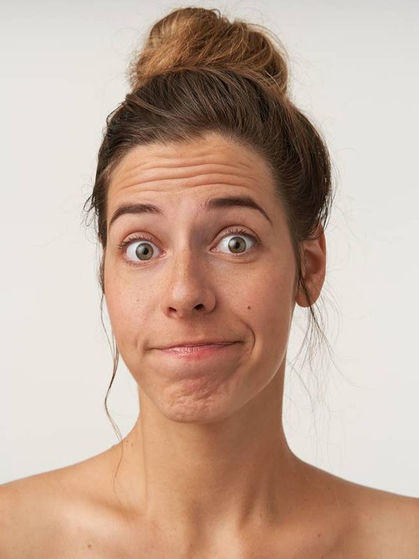 Close-up of attractive young woman posing over white background with bewildered face, wearing bun hairstyle and no make-up, wrinkling forehead and pursing lips