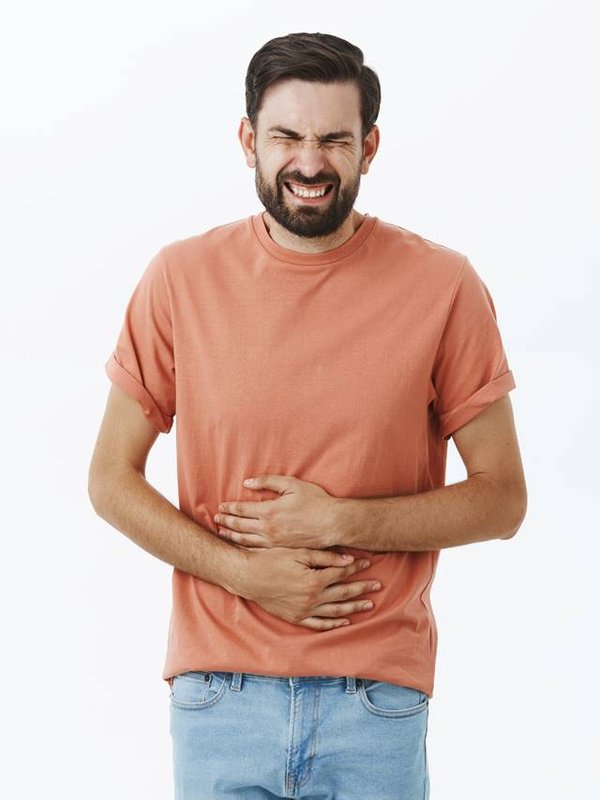 Guy regrets eating fast food feeling pain in stomach clenching teeth and closing eyes from pain touching belly suffering disorder or stomachache waiting for ambulance posing against gray background