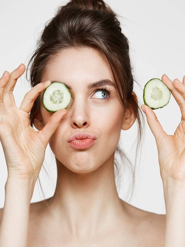 Young beautiful naked girl smiling hiding eye behind cucumber slice over white background. Beauty spa and cosmetology concept.
