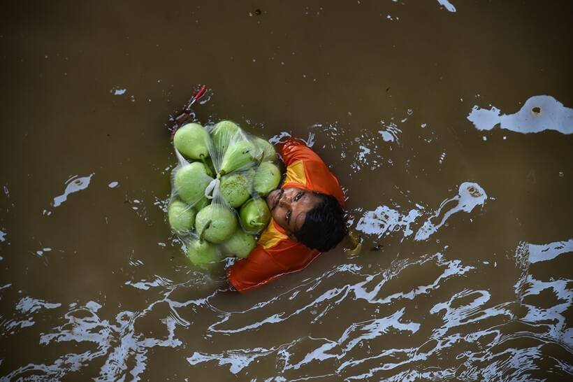 लौकी ले जा रहा एक व्यक्ति गुरुवार को यमुना नदी के पास बाढ़ वाले इलाके से होकर गुजरता है। (PTI)