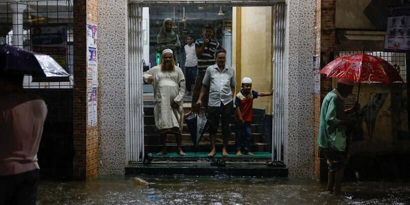 People wait on the gate of a mosque as streets are flooded before the Cyclone Sitrang hits in Dhaka
