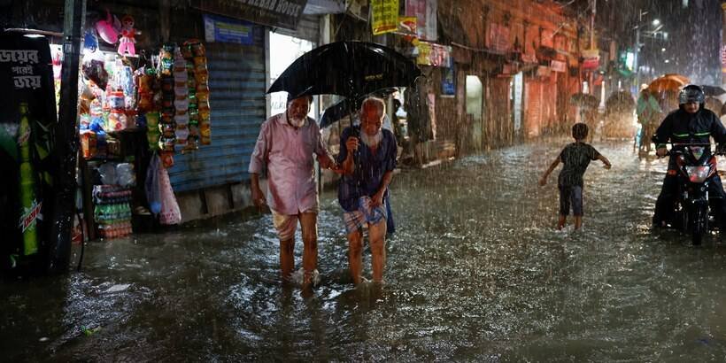 People wade through a flooded street amid continuous rain before the Cyclone Sitrang hits in Dhaka