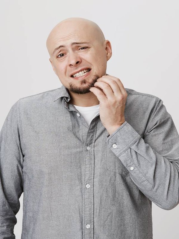Headshot of clueless bald bearded caucasian man looking at camera with confused and puzzled expression, frowning, having forgot about something, scratching his beard. Face expression and emotions