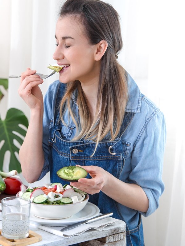 Young and happy woman eating salad at the table