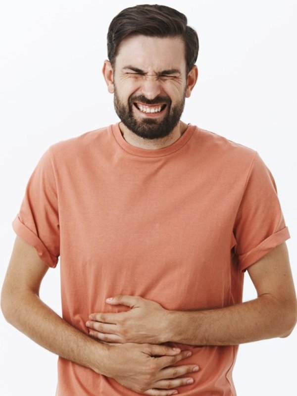 Guy regrets eating fast food feeling pain in stomach clenching teeth and closing eyes from pain touching belly suffering disorder or stomachache waiting for ambulance posing against gray background