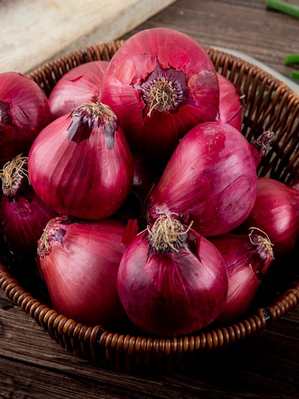 side view of basket full of red onions on wooden background