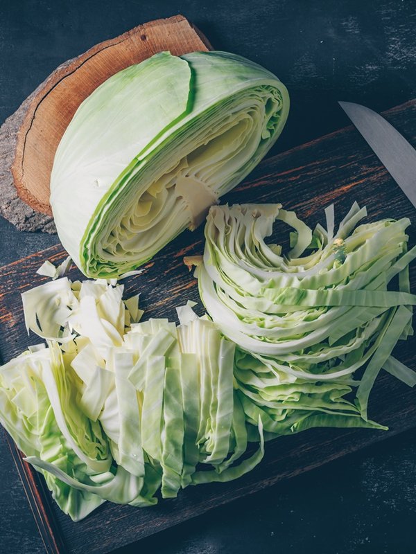 Flat lay sliced and chopped cabbage in cutting board and knife with wood stub on dark textured background. horizontal