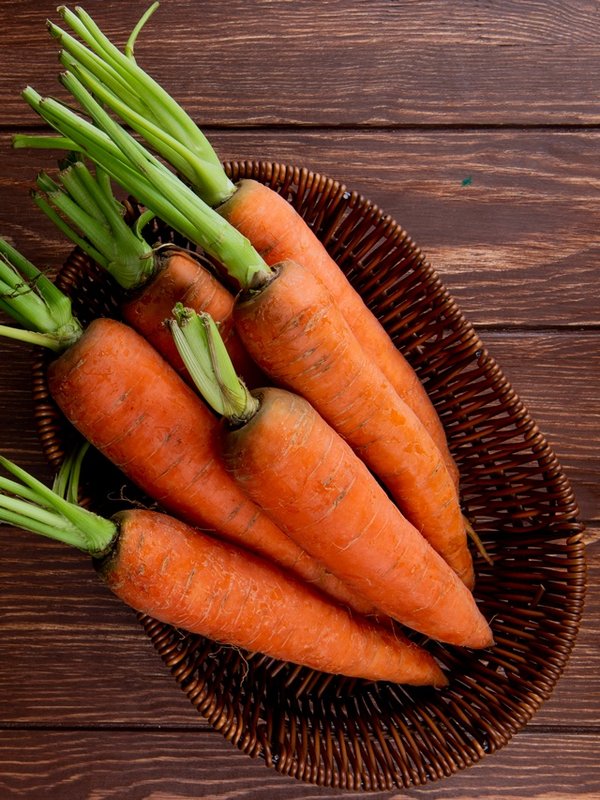 top view of basket plate with carrots on wooden background with copy space