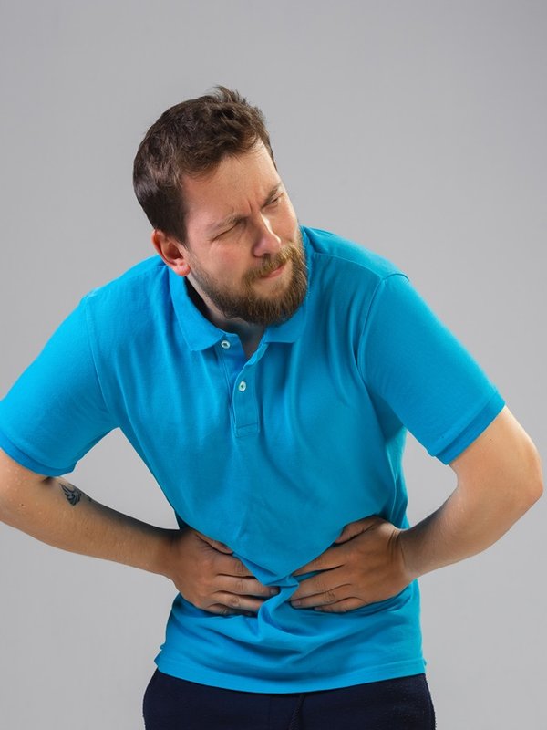 Young man suffers from pain, feels sick, ill and weakness isolted on studio background