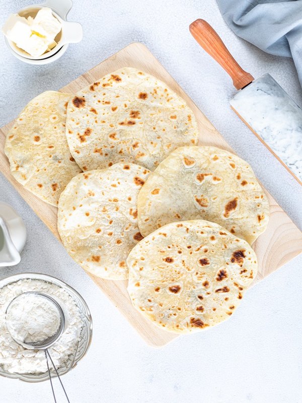Homemade wheat tortillas, pita bread, tortilla, pita with ingredients for cooking on a white table. Top view. Vertical