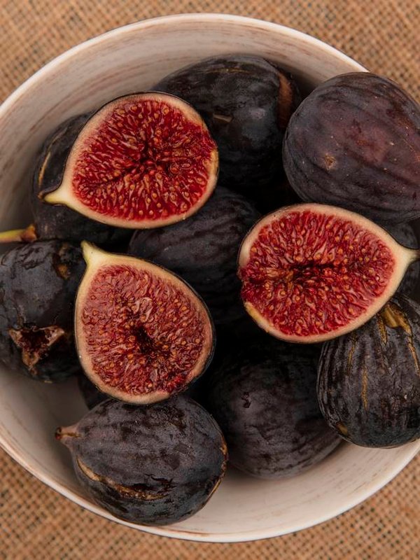 top view of sweet ripe black mission figs on a bowl on a sack cloth on a blue background