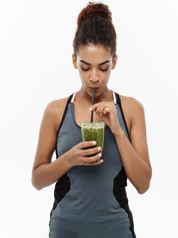 Healthy and Fitness concept - Beautiful American African lady in fitness clothing drinking healthy vegetable drink. Isolated on white background.