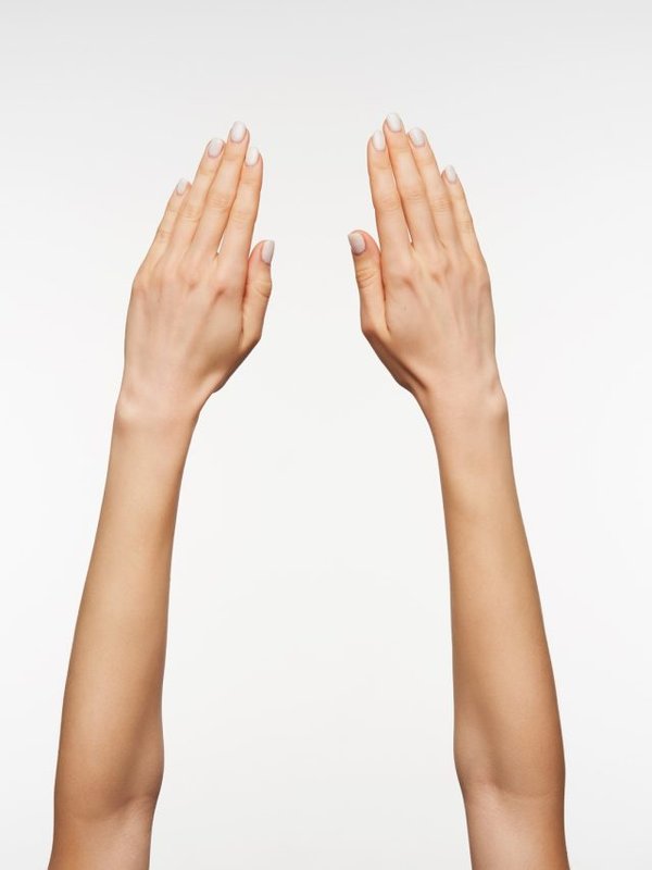 Close-up of beautiful woman's hand with manicure keeping fingers together while posing against white background, hand symbol viewed from back