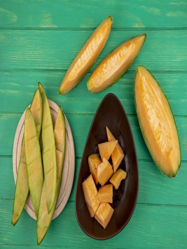top view of peels of melon on a wooden kitchen board with slices of melon on a brown bowl