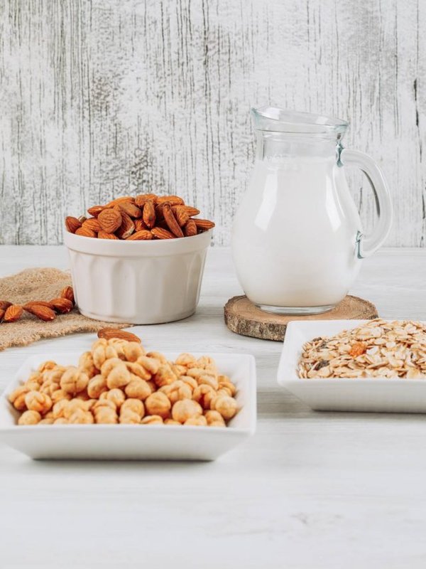 Side view milk carafe with bowl of almonds, hazelnut, and oats on white wooden background. vertical