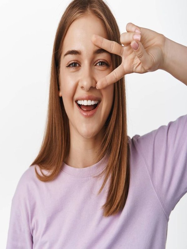 Close up portrait of natural young woman, candid smile of girl showing peace v-sign near eye, concept of woman beauty and face expressions, white background